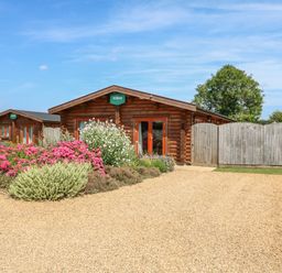 A gravel driveway with flower beds and wooden cabins behind a wooden fence at Willow Lodge in Greetham Rutland