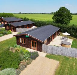 A group of wooden lodges with paved patios and garden furniture set in a grassy area with hedges and fields in the background at Willow Lodge in Greetham Rutland
