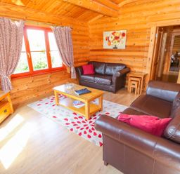 A living room with brown leather sofas a wooden coffee table a television and patterned curtains at Sycamore Lodge in Greetham Rutland