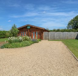 A wooden cabin with a gravel driveway and garden at Sycamore Lodge in Greetham Rutland