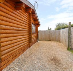 An exterior side view of a log cabin with gravel ground and wooden fencing at Church View in Greetham Rutland
