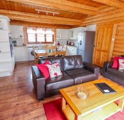 A living area with two brown sofas and a wooden coffee table next to a kitchen with white cabinets and a dining table at Church View in Greetham Rutland