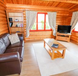 A living room with a leather sofa a wooden coffee table a bookshelf and a television at Cedar Lodge in Greetham Rutland