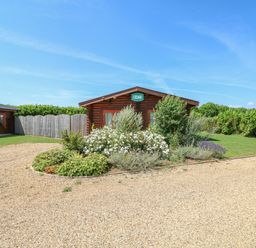 A log cabin with a garden of shrubs and flowers in front at Cedar Lodge in Greetham Rutland