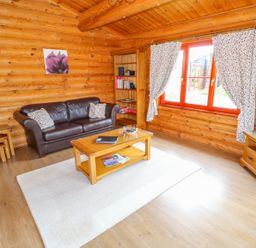 A living room with a brown leather sofa wooden coffee table bookshelves and a television at Beech Lodge in Greetham Rutland