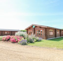 A wooden cabin with flowers and a gravel pathway at Beech Lodge in Greetham Rutland