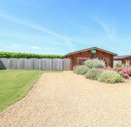 A gravel driveway leading to wooden lodges with plants and grass at Beech Lodge in Greetham Rutland