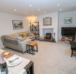 A living room with a gray sofa and yellow cushions a wood burning stove and a TV at Wynding Apartment in Amble-By-The-Sea