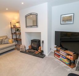 A living room with a sofa cushions a fireplace with wood a television on a stand with board games and a shelving unit with a lamp at Wynding Apartment in Amble-By-The-Sea