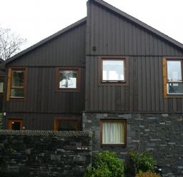 A house with dark wooden upper walls and stone lower walls with several windows and a small garden in front at 13 Keswick Bridge in Keswick