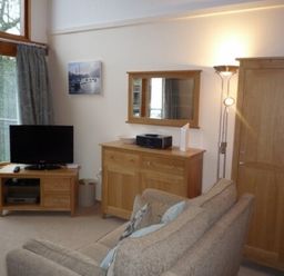 A living room with a beige sofa television on wooden stand wooden cabinet floor lamp and a large window at 13 Keswick Bridge in Keswick