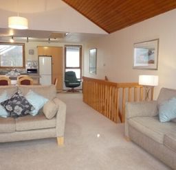 A living room with sofas and cushions next to a kitchen and a wooden railing at 13 Keswick Bridge in Keswick