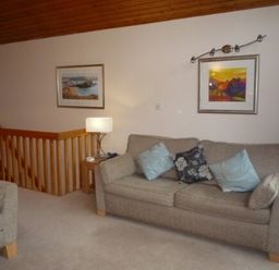 A living room with a sofa and armchair cushions a lamp and framed paintings on the walls at 10 Keswick Bridge in Keswick