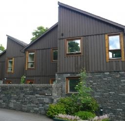A row of modern houses with wood paneling and stone walls with some greenery at 16 Keswick Bridge in Keswick