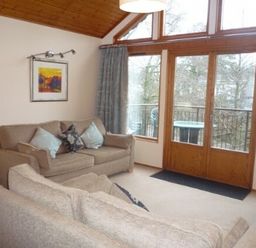 A living room with two beige sofas and large windows with a door leading to a balcony at 16 Keswick Bridge in Keswick