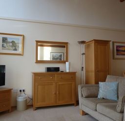 A living room with a beige sofa and blue cushions wooden cabinets and a television at 16 Keswick Bridge in Keswick