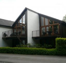 A two-story building with balconies and outdoor chairs surrounded by greenery at 6 Keswick Bridge in Keswick