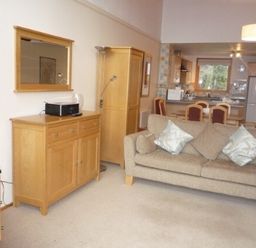 A living room with a beige sofa and wooden furniture including a sideboard wardrobe and dining table at 20 Keswick Bridge in Keswick