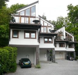 Three modern white houses with balconies and cars parked under them surrounded by trees and greenery at 21 Keswick Bridge in Keswick