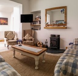 A living room with armchairs and sofas around a wooden coffee table near a wood stove with a mirror above at Angorfa in Cemaes Bay