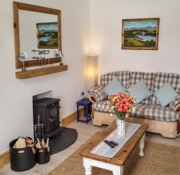 A living room with a checked sofa blue cushions a wooden coffee table with flowers a fireplace and a large mirror at Angorfa in Cemaes Bay