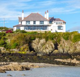 A large house on a cliff overlooking a rocky beach and water at Angorfa in Cemaes Bay