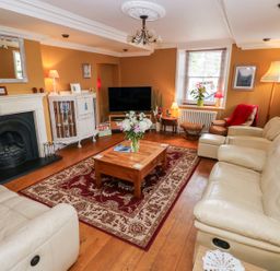A living room with beige sofas a wooden coffee table with flowers a large rug a fireplace and a television at Castle School House in Kidwelly