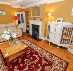 A living room with a beige sofa wooden coffee table flowers fireplace and white cabinet at Castle School House in Kidwelly