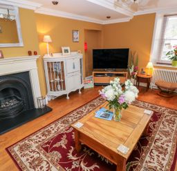 A living room with a wooden coffee table with flowers and books on a red patterned rug and a television at Castle School House in Kidwelly