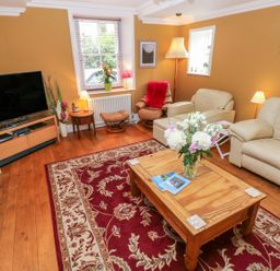 A living room with beige leather sofas a wooden coffee table with flowers and a red patterned rug at Castle School House in Kidwelly
