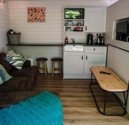 A living room with a sofa and kitchenette at Reflection in Longtown