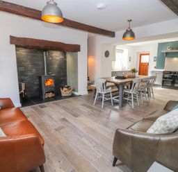 A living room with two sofas and a wood burning stove next to a dining table with chairs at Llys Alaw in Llangernyw