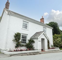 A white two-story house with two chimneys and climbing plants by the windows at Llys Alaw in Llangernyw