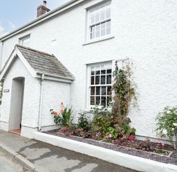 The exterior of a white textured house with two windows a small entrance porch and a flower bed along the wall at Llys Alaw in Llangernyw