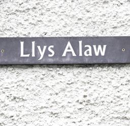 A black rectangular sign with white text reading Llys Alaw mounted on a white textured wall at Llys Alaw in Llangernyw