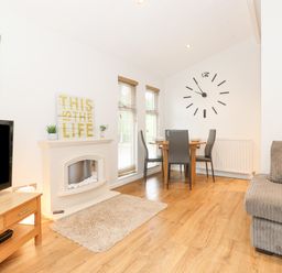 A dining area with table and chairs next to a wall clock and a living room with a TV wooden stand and fireplace at 10 Thirlmere White Cross Bay near Troutbeck Bridge