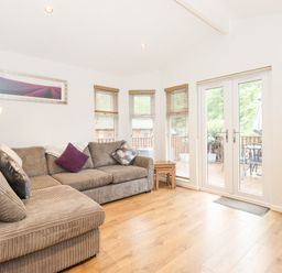 A living room with a brown sectional sofa and pillows beside windows and glass doors leading to a deck at 10 Thirlmere White Cross Bay near Troutbeck Bridge