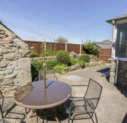 An outdoor patio with a round table and four chairs next to stone walls and a garden at Ty Uchaf in Dyffryn Ardudwy
