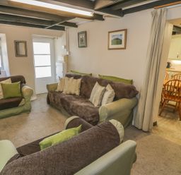 A living room with sofas and cushions a television and an adjoining kitchen with a dining table and chairs at Ty Uchaf in Dyffryn Ardudwy