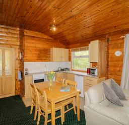 A kitchen and dining area with wooden table and chairs a white leather sofa and wood panel walls at Eagle Lodge in Strathpeffer
