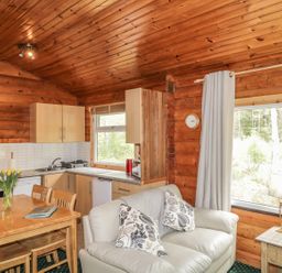 A kitchen and dining area with wooden table and chairs and a small sofa near a window at Otter Lodge in Strathpeffer