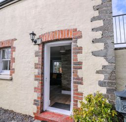 An exterior wall with a door and window framed in red bricks and a black lamp above the door at Bwthyn Y Jacdo in Crymych