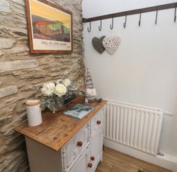 A corner with a wooden cabinet a radiator a wall-mounted coat rack and decorative items at Bwthyn Y Jacdo in Crymych