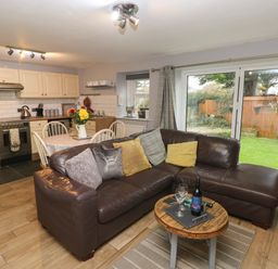 An open plan kitchen and living area with a brown leather sofa and a small round wooden table with wine and glasses at Bwthyn Y Jacdo in Crymych