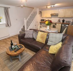 A living area with a brown leather sofa, wooden coffee table, round dining table with chairs, and kitchen with cream cabinets at Bwthyn Y Jacdo in Crymych