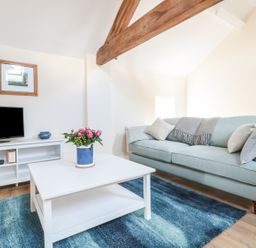 A living room with a blue sofa and a white coffee table with flowers on it at Granary 2 in Madley