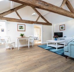 A living room with wooden beams white walls and furniture including a sofa coffee table TV and dining table at Granary 2 in Madley
