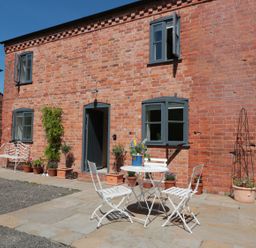 A brick house with blue framed windows and a door with outdoor white table and chairs and potted plants on a patio at Granary 1 in Madley near Hereford