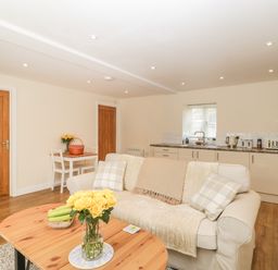 An open plan living room and kitchen with a beige sofa and wooden coffee table at Granary 1 in Madley near Hereford