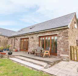 An outdoor stone patio with potted plants and two wooden chairs outside a stone house at The Barn in Abergavenny